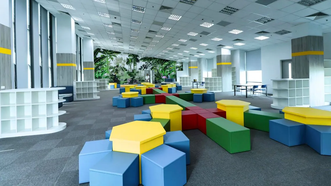 Ambiente scolastico con sedute colorate, scaffali e grandi finestre