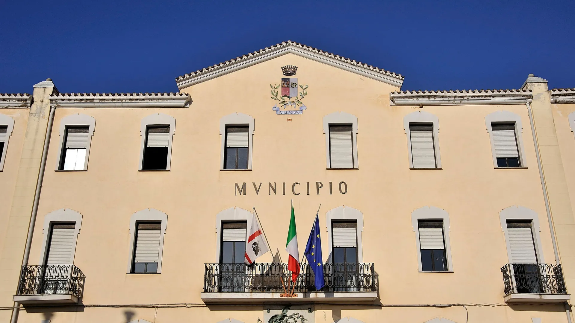 Facciata del municipio di Villacidro con stemma comunale e bandiere sul balcone