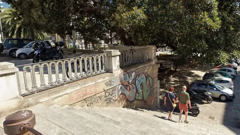 Scalinata con parapetti in pietra e metallo, alberi e passanti.